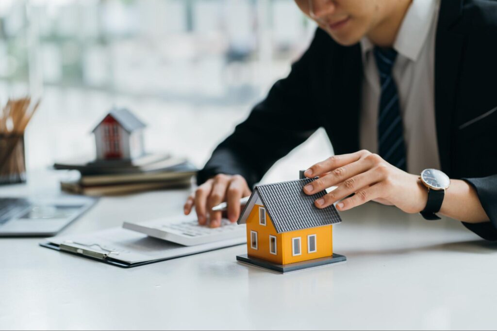 man using a calculator while holding a miniature house